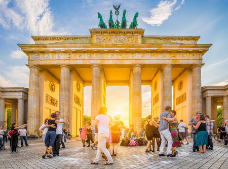 People dancing in front of famous Brandenburg Gate, a symbol for peace and unity and historic landmark, in golden evening light at sunset with blue sky in summer, Berlin, Germanyのeditorial素材