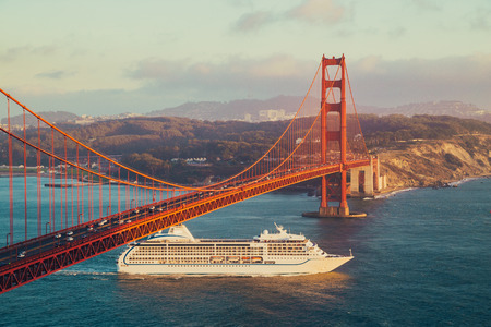 Beautiful panorama view of cruise ship passing famous Golden Gate Bridge with the skyline of San Francisco in the background in beautiful golden evening light at sunset in summer, California, USAの写真素材