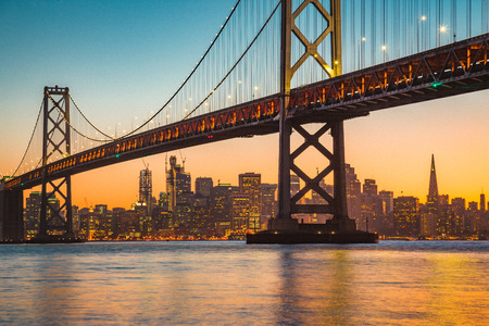 Classic panoramic view of San Francisco skyline with famous Oakland Bay Bridge illuminated in beautiful golden eveningの写真素材