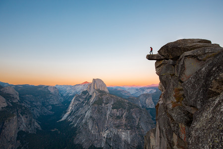 A fearless hiker is standing on an overhanging rock enjoying the view towards famous Half Dome at Glacier Pointの写真素材