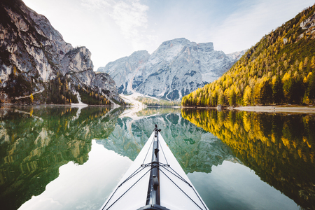 Beautiful view of kayak on a calm lake with amazing reflections of mountain peaks and trees with yellow autumn foliage in fall, Lago di Braies, Italyの写真素材