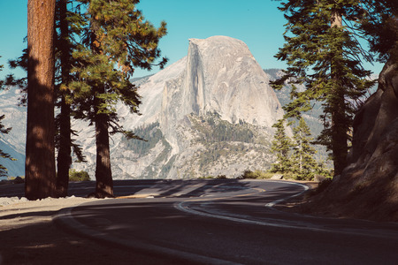 Beautiful view of winding Glacier Point Road with famous Half Dome summit in golden evening light at sunset, Yosemite National Park, California, USAの写真素材