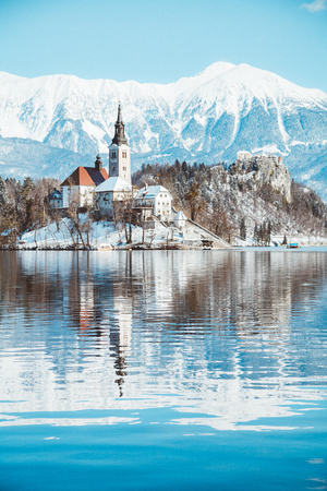 Beautiful view of famous Bled Island (Blejski otok) at scenic Lake Bled with Bled Castle (Blejski grad) and Julian Alps in the background in golden morning light at sunrise in winter, Slovenia.のeditorial素材