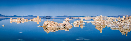 Panoramic view of fascinating tufa rock formations mirrored on calm water surface of famous Mono Lake on a beautiful sunny day with blue sky in summer, Mono County, California, USAの写真素材