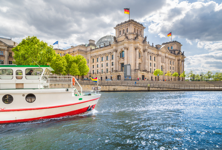 Panoramic view of Berlin government district with excursion boat on Spree river passing famous Reichstag building and Paul Lobe Haus on a sunny day with blue sky and clouds, Berlin Mitte, Germanyの写真素材