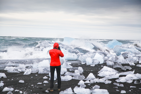 Hiker watching waves crash against icebergs at famous Diamond Beach, Jokulsarlon glacier lagoon, Vatnajokull National Park, Icelandの写真素材