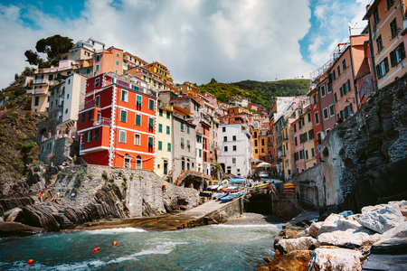 Classic view of beautiful Riomaggiore, one of the five famous picturesque fisherman villages of Cinque Terre, on a sunny day with blue sky and clouds in summer, Liguria, Italyの写真素材