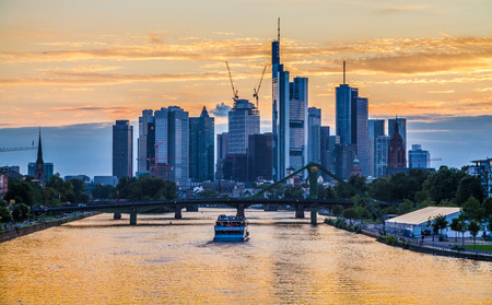 Classic panoramic view of famous Frankfurt am Main skyline with dramatic clouds and passenger ship in beautiful golden post sunset twilight during blue hour at dusk, Hessen, Germanyの写真素材