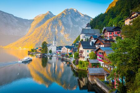 Classic postcard view of famous Hallstatt lakeside town in the Alps with traditional passenger ship in early morning light at sunrise on a beautiful day in summer, Salzkammergut region, Austriaの写真素材