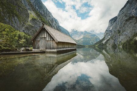 Idyllic view of traditional old wooden boat house at scenic Lake Obersee on a beautiful sunny day with blue sky and clouds in summer, Nationalpark Berchtesgadener Land, Bavaria, Germanyの写真素材