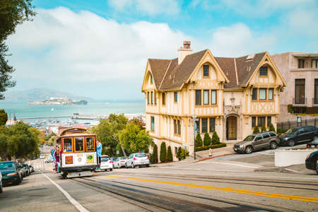 Powell-Hyde cable car climbing up steep hill in central San Francisco with famous Alcatraz Island in the background on a sunny day with blue sky, USA.のeditorial素材