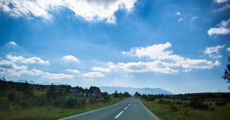Driving a car on a highway surrounded with trees , with a beautiful sky and mountains in the backgroundの写真素材
