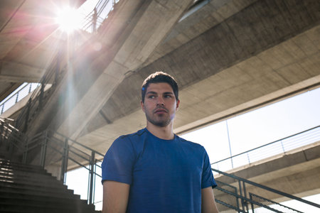 Young male runner standing in an urban scene, preparing for a run