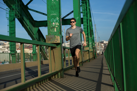Handsome male runner jogging on a bridge, urban sceneryの写真素材