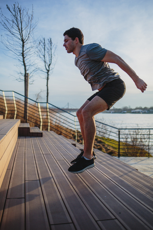 Male athlete doing box jumps in an urban scenery, beside a riverの写真素材