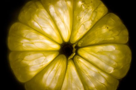 Yellow slice of lemon in transparent light on black backgroundの写真素材