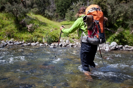 Young woman with backpack crossing mountain streamの写真素材