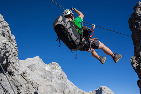 Young man going accross tyrolean traverse on via ferrata  Klettersteig 