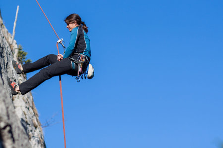 Young woman abseiling steep rock face