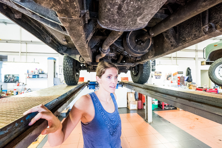 Young woman in the workshop with car chassis aboveの写真素材