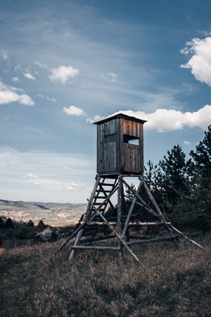 Wooden hunting lookout tower standing in a meadow with scenic countryside view and blue sky...