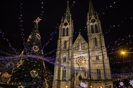 The festive lights of NÃ¡mÄstÃ­ MÃ­ru glow warmly, highlighting St. Ludmila Basilica beside a beautifully decorated Christmas tree.の写真素材