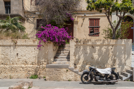 Rhodes Town, Greece. 05/30/2018. BMW R12 motorcycle covered in white towel to protect from scorching sun. Parked in front of derelict residential medieval dwelling in historical part of downtown. Island of Rhodes. Greece. Europe.のeditorial素材