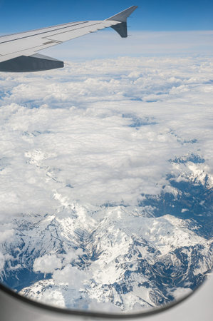 View from airborne airplane window at cloudy sky and Alps mountains with snow covered peaks from...