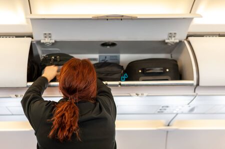 Female passenger reaching out to her luggage in overhead airplane compartment.の写真素材