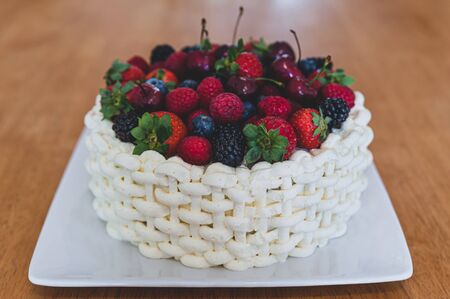 Top view at beautiful summer cake decorated with berries on white plate sitting on wooden surface.の写真素材