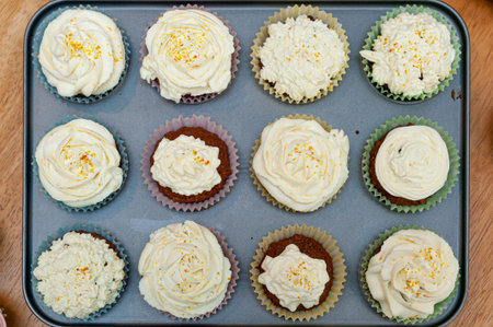 Home baked cupcakes beautifully decorated with buttercream on top placed in baking tin.