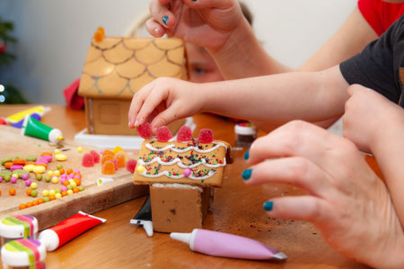 Family of three decorating home baked gingerbread houses with colorful sweet pastilles and sparkling...