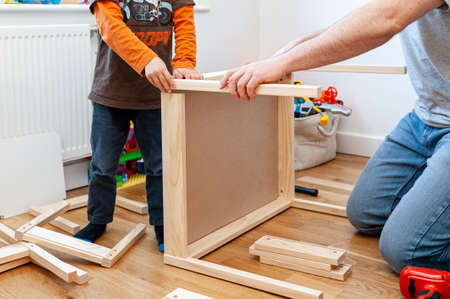 A male parent with son working on assembling  flat-pack furniture for boy's room. A set of two small chairs with little desk.の写真素材