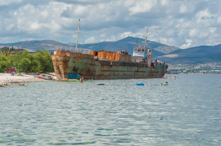 Shipwreck washed ashore spoiling Adratic Sea coastline. Locals and tourist swimming and sunbathing next to remains of beached vessel.のeditorial素材