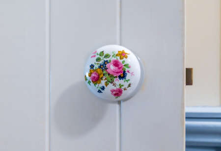 Close-up at Victorian style round porcelain floral decorated door knob on white wooden barn style door.の写真素材