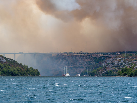 Forest fire in Croatia, summer natural disaster close to national park Krka, Sibenik region, boats and yachts escaping Skradin town from the smokeの写真素材