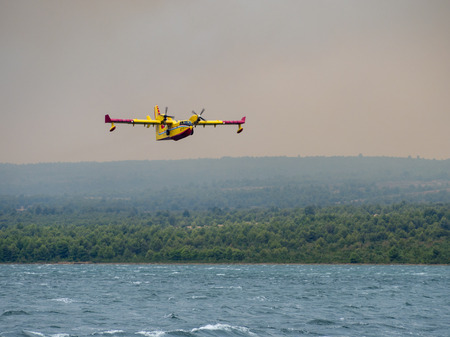 Firefighter airplane, water bomber, air tank taking water from the sea and extinguishing forest fire in Croatia, close to Krka national park and Skradin town, Sibenik regionの写真素材