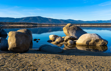 big stone or rock in lake or see with mountains in background and sand in frontの写真素材