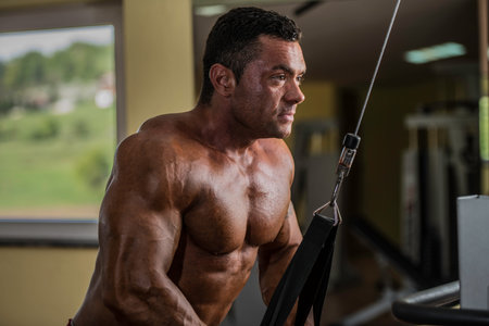 bodybuilder doing heavy weight exercise for triceps with cable