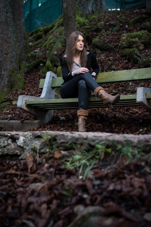 young woman in jacket sitting at the benchの写真素材
