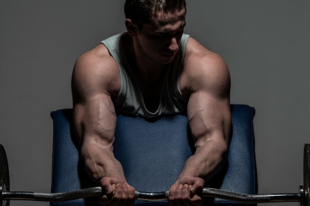 young bodybuilder doing heavy weight exercise for biceps with barbellの写真素材