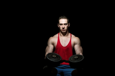 young bodybuilder posing with dumbbell at the bench on black backgroundの写真素材