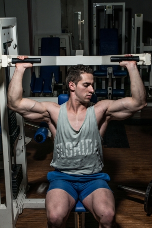 young bodybuilder doing shoulder press on machineの写真素材
