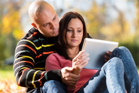 Male And Female Look At Electronic Tablet In Parkの写真素材