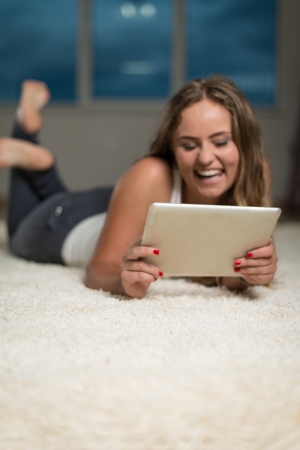 Young Woman With Digital Tablet Lying on Carpetの写真素材