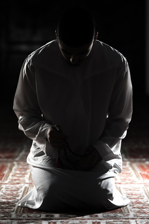 Young Muslim Man Making Traditional Prayer To God While Wearing A Traditional Cap Dishdashaの写真素材