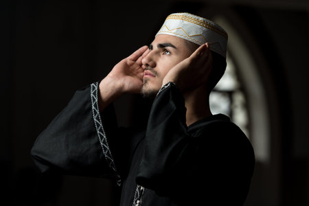 Young Muslim Guy Making Traditional Prayer To God While Wearing A Traditional Cap Dishdasha