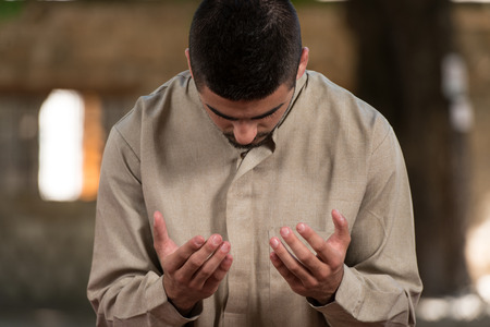 Young Muslim Man Making Traditional Prayer To God While Wearing A Traditional Cap Dishdashaの写真素材