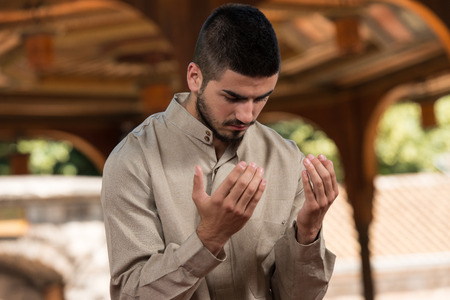 Young Muslim Man Making Traditional Prayer To God While Wearing A Traditional Cap Dishdashaの写真素材