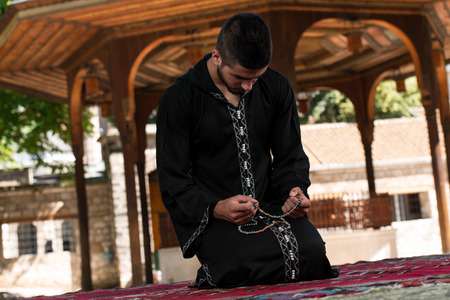 Young Muslim Man Making Traditional Prayer To God While Wearing A Traditional Cap Dishdashaの写真素材
